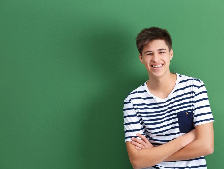 Happy teenage boy in casual clothes on color background