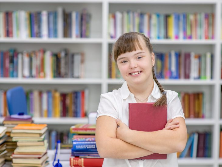 Portrait of a smiling girl with syndrome down at library. Empty space for text. Education for disabled children concept